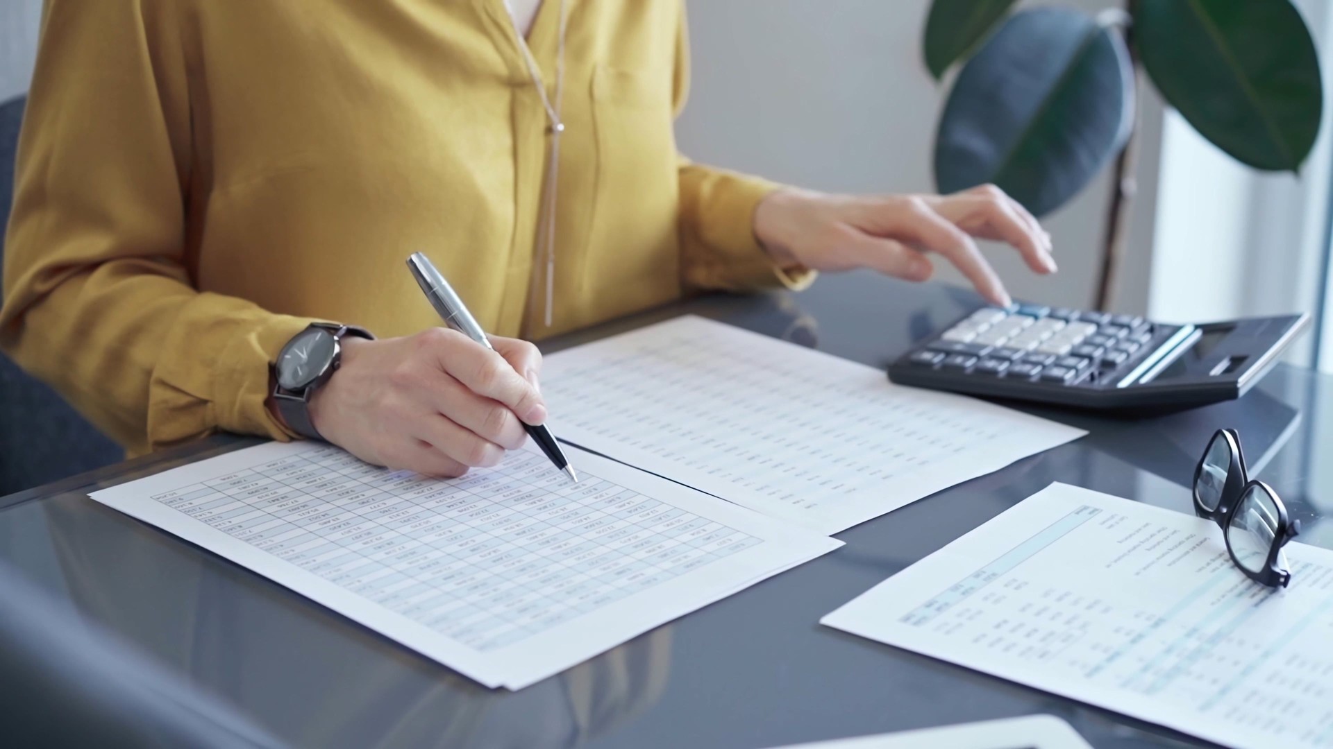 Professional business woman in yellow blouse is working on financial reports. Close-up of a woman's hands using calculator for audit or accounting
